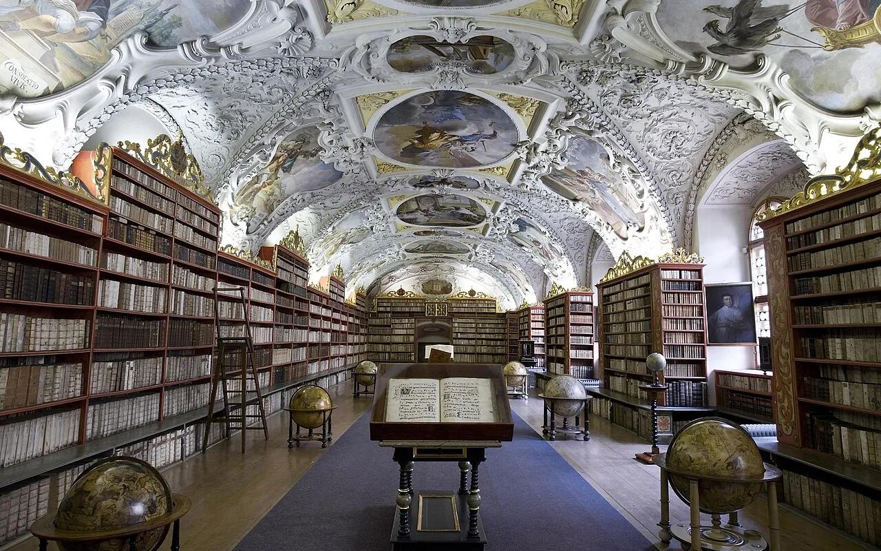 The Theological Hall at Strahov Library, gilded stucco bookcases lining both walls beneath a painted ceiling, seen from the entrance doorway